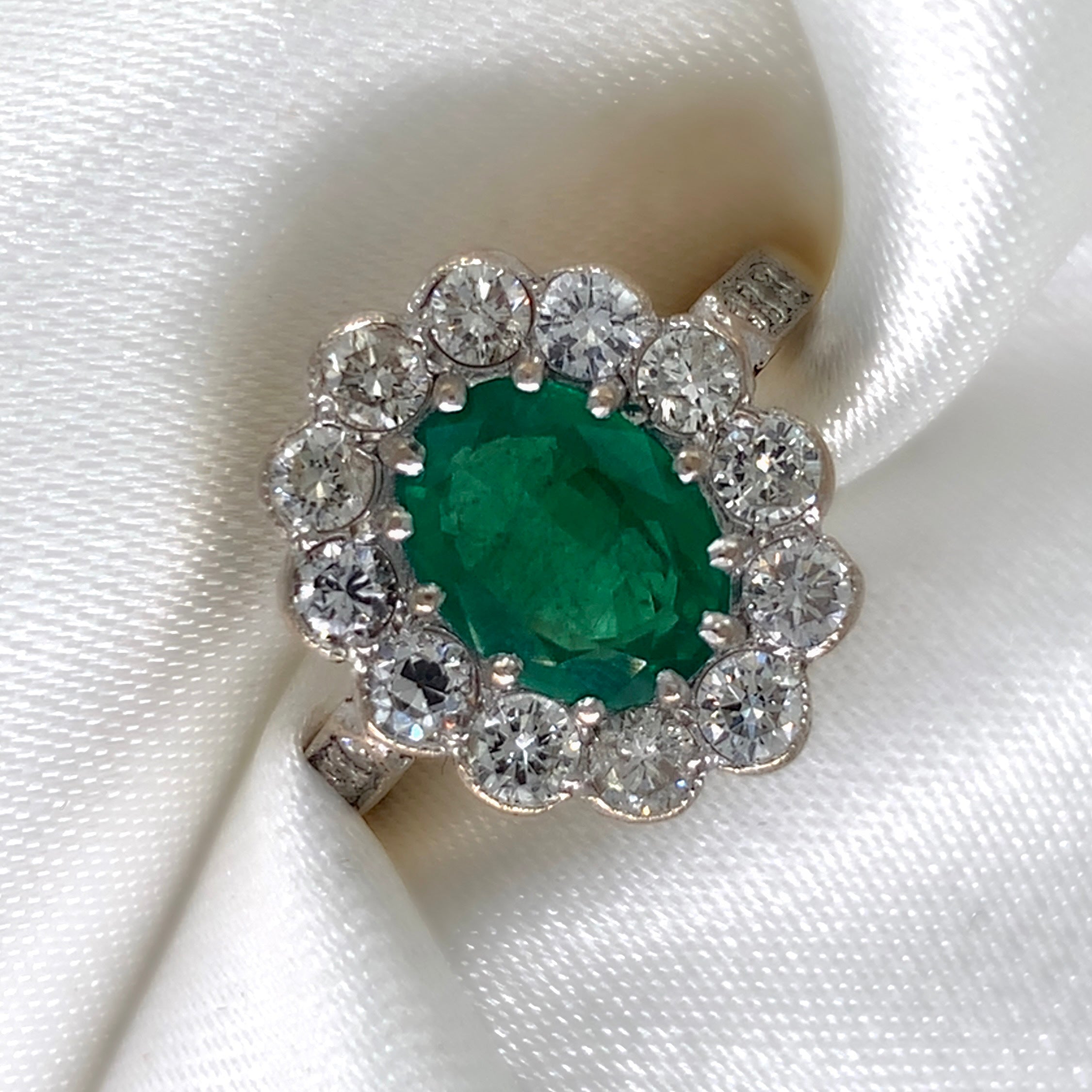 1940s emerald and diamond cluster ring with a classic Art Deco design, featuring a central emerald surrounded by a halo of diamonds.