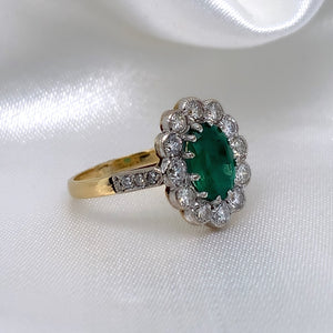 A side view of a 1940s emerald and diamond cluster ring with a classic Art Deco design, featuring a central emerald surrounded by a halo of diamonds.