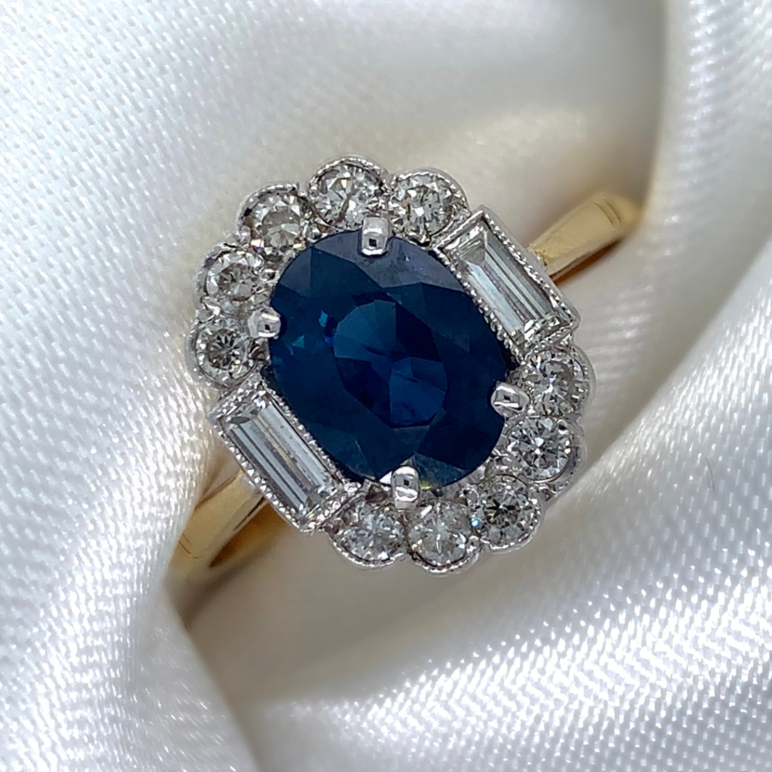 1980s Art Deco ring with a deep blue oval-cut sapphire surrounded by a halo of sparkling diamonds featuring a vibrant sapphire and a platinum and 18ct yellow gold setting