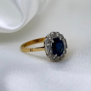 A side view of a 1980s Art Deco ring with a deep blue oval-cut sapphire surrounded by a halo of sparkling diamonds featuring a vibrant sapphire and a platinum and 18ct yellow gold setting
