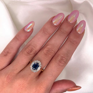 A 1980s Art Deco ring with a deep blue oval-cut sapphire surrounded by a halo of sparkling diamonds featuring a vibrant sapphire and a platinum and 18ct yellow gold setting on a hand.