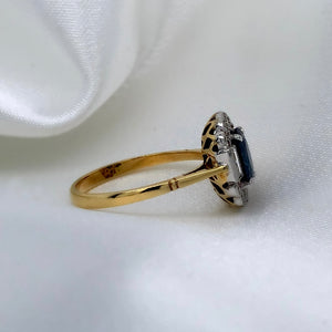 A side view of a 1980s Art Deco ring with a deep blue oval-cut sapphire surrounded by a halo of sparkling diamonds featuring a vibrant sapphire and a platinum and 18ct yellow gold setting