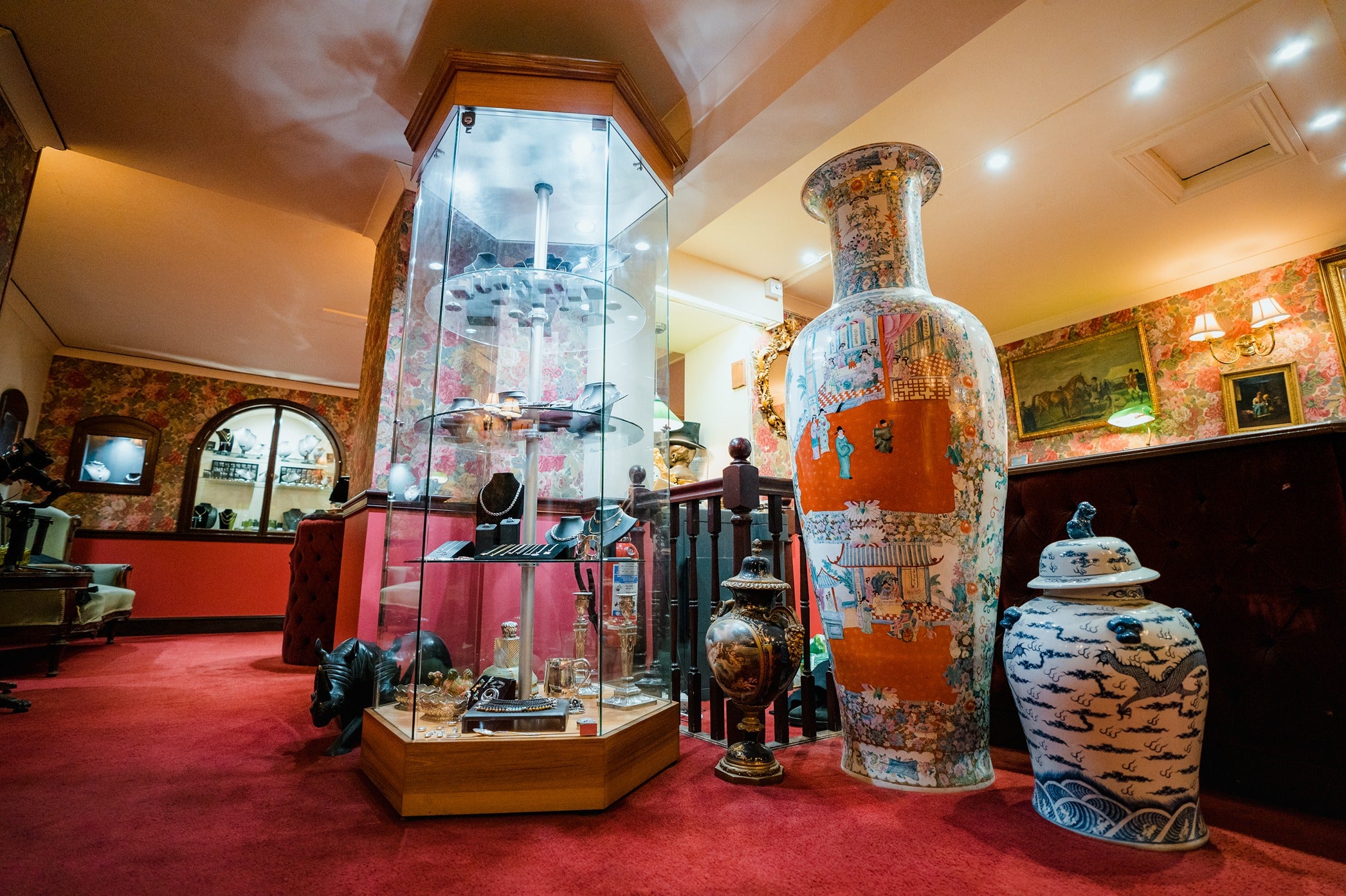 A corner of the Ebony Jewellers showroom showcasing a floor-to-ceiling glass tower display case filled with silver and gold jewellery. Next to it stands a collection of oversized oriental porcelain vases with intricate blue and orange patterns.