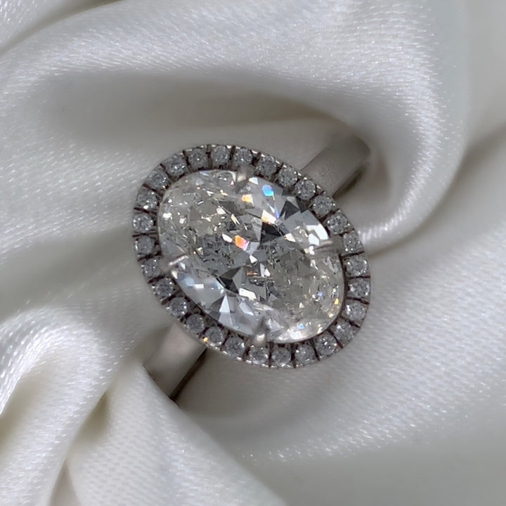 Platinum engagement ring featuring an oval cut diamond center stone encircled by a sparkling halo of round diamonds