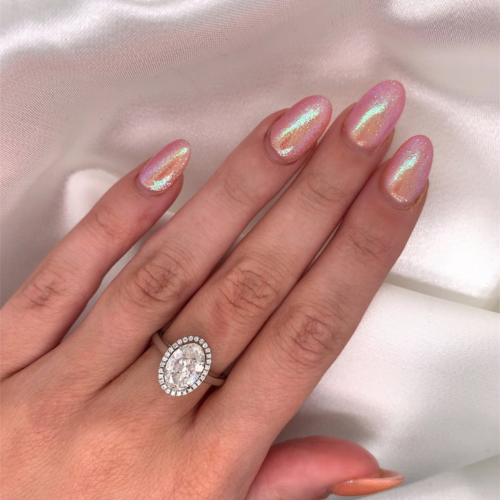 Platinum engagement ring featuring an oval cut diamond center stone encircled by a sparkling halo of round diamonds on a hand.