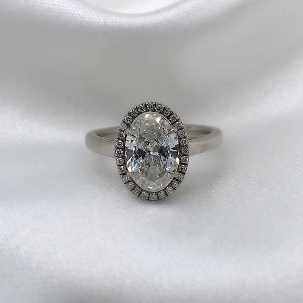 Platinum engagement ring featuring an oval cut diamond center stone encircled by a sparkling halo of round diamonds