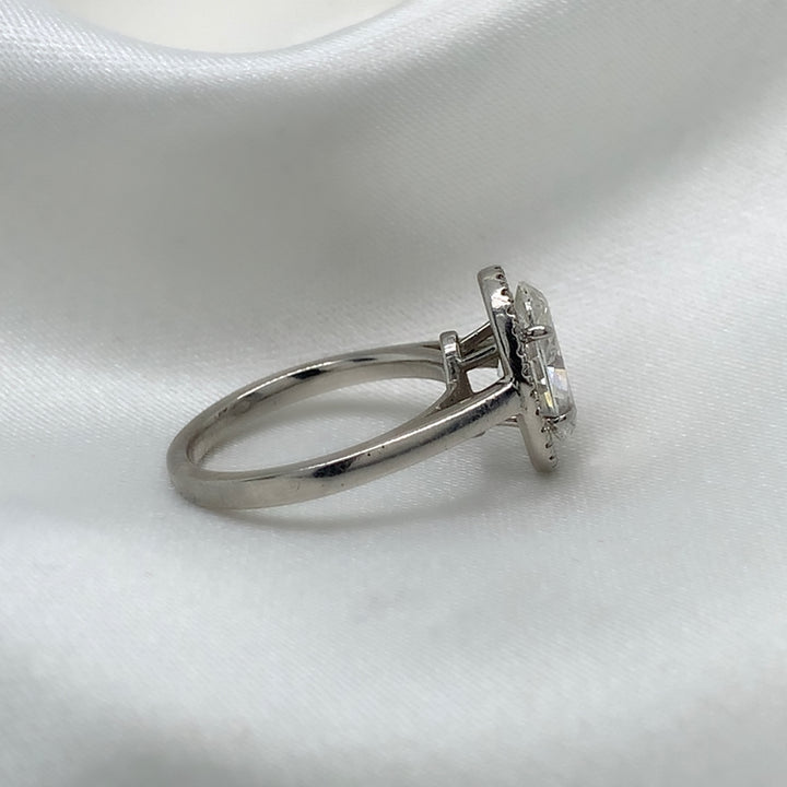 A side view of a platinum engagement ring featuring an oval cut diamond center stone encircled by a sparkling halo of round diamonds