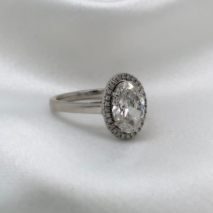 A side view of a platinum engagement ring featuring an oval cut diamond center stone encircled by a sparkling halo of round diamonds