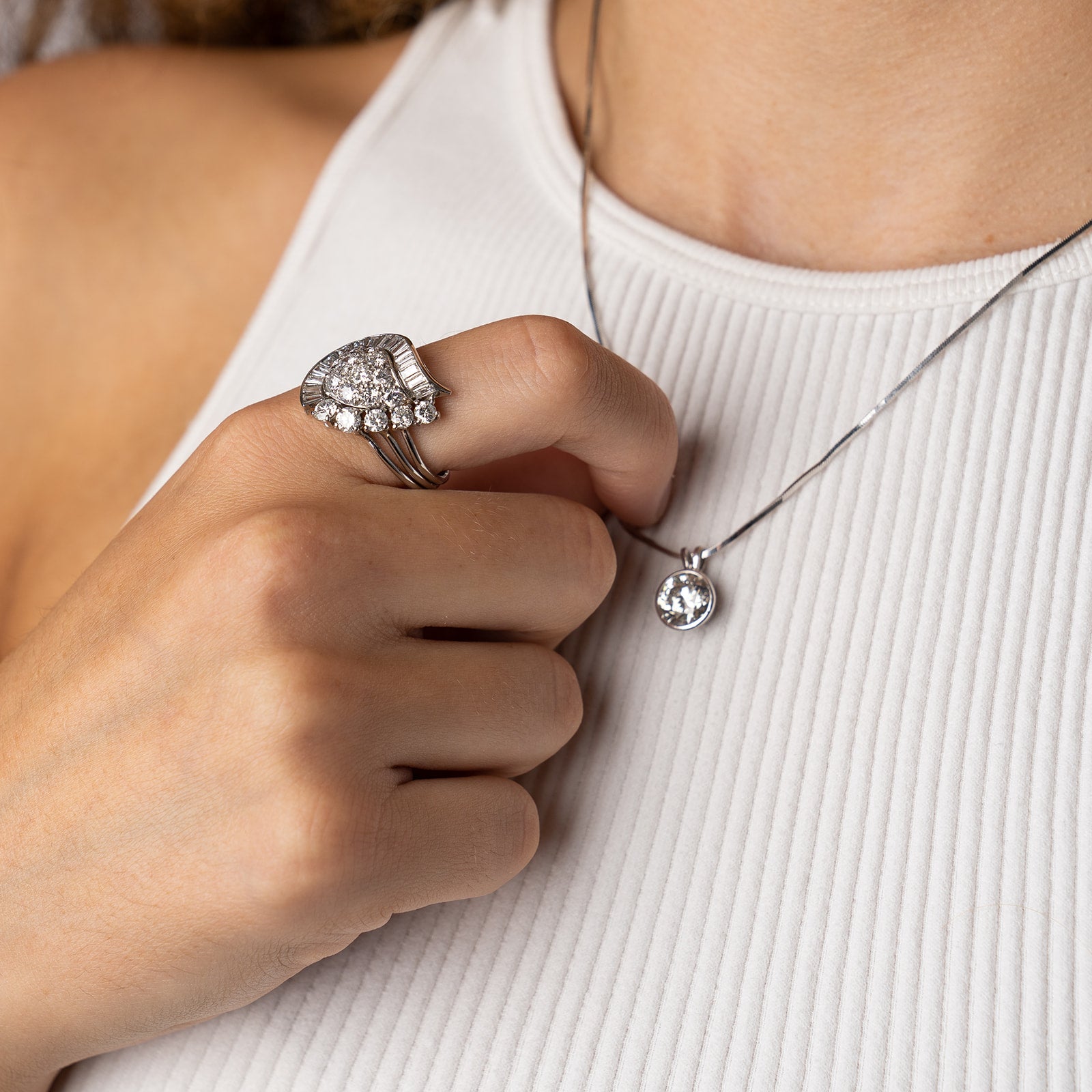 A sophisticated jewellery pairing including an art deco-style diamond cocktail ring with a fanned baguette border and a simple solitaire diamond pendant on a delicate white gold chain.