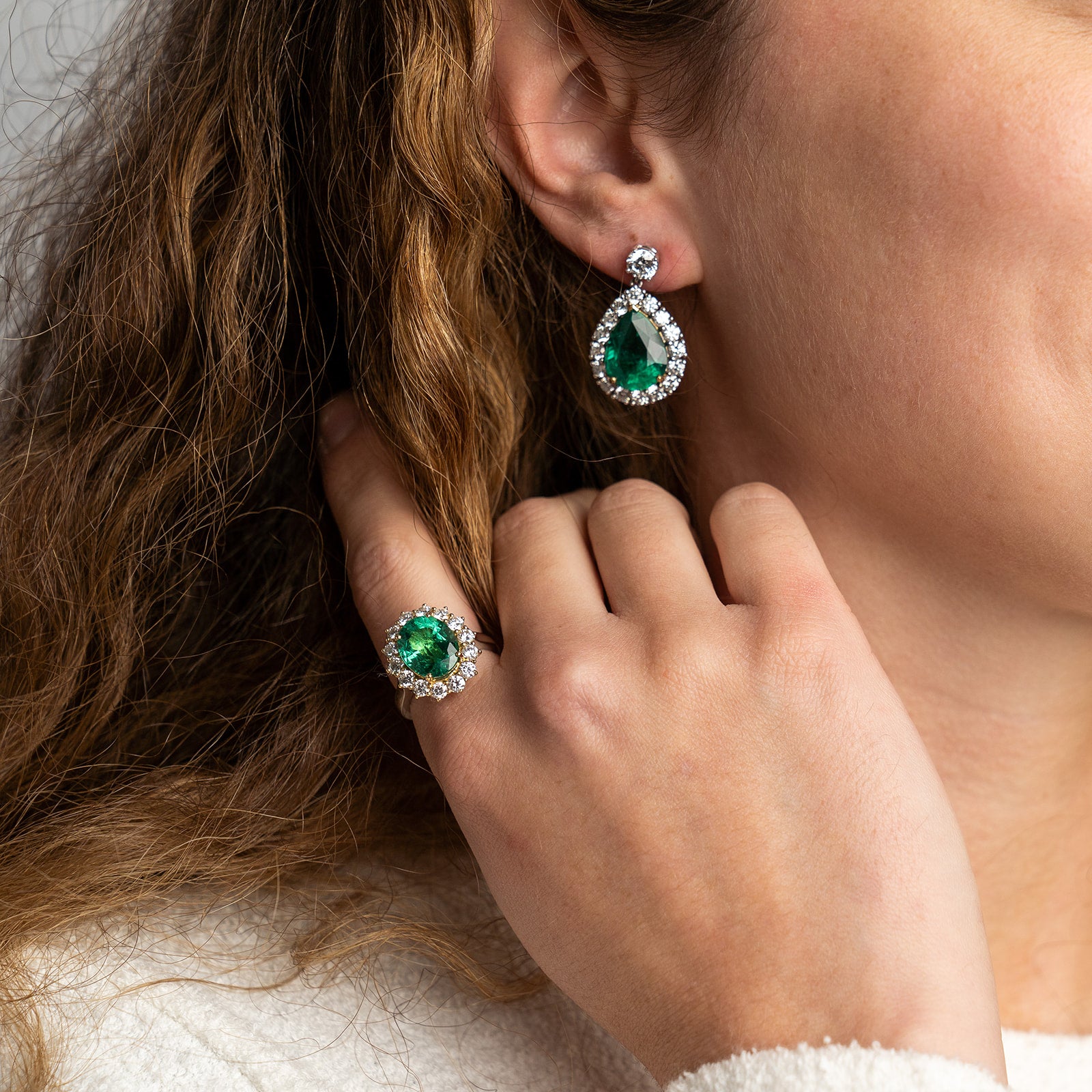 A matching emerald jewellery set consisting of a large oval emerald halo ring and coordinating pear-shaped emerald drop earrings.