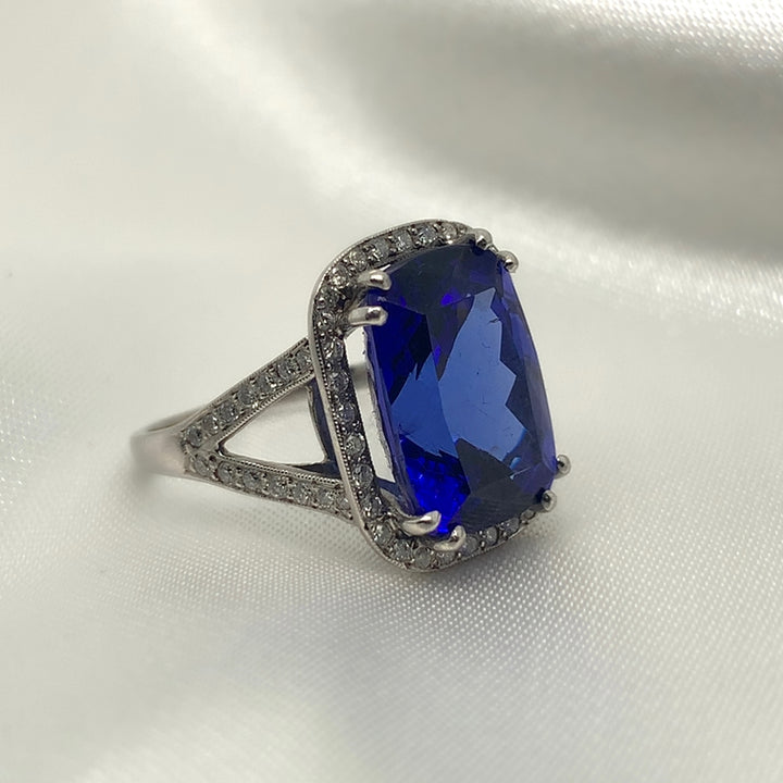 A side view of a stunning radiant-cut tanzanite ring set in platinum with a halo of sparkling diamonds.