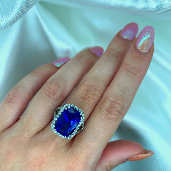 A stunning radiant-cut tanzanite ring set in platinum with a halo of sparkling diamonds, shown on a hand.