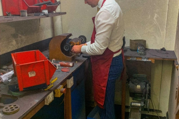 An expert jeweller (Cian Griffin) at work in the Ebony Jewellers workshop, wearing a red apron and white shirt while using a bench-mounted polishing motor. This process illustrates the professional cleaning, polishing, and plating services used to restore the original lustre of fine jewellery.