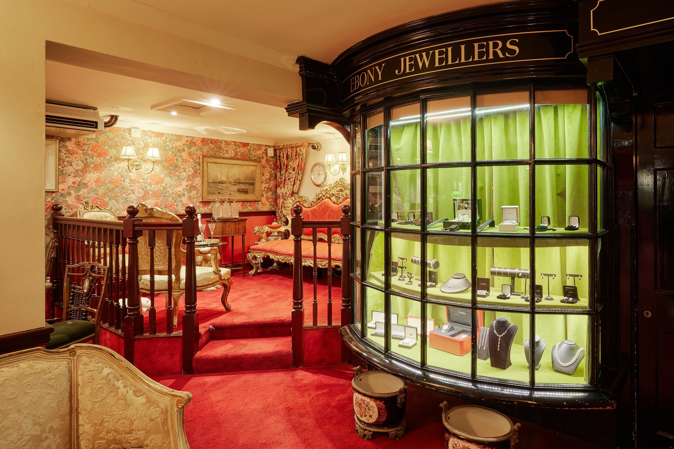 An interior view of the signature curved glass "Ebony Jewellers" window display. The display is backed with vibrant lime-green fabric, beautifully highlighting an array of fine jewellery, watches, and necklaces.