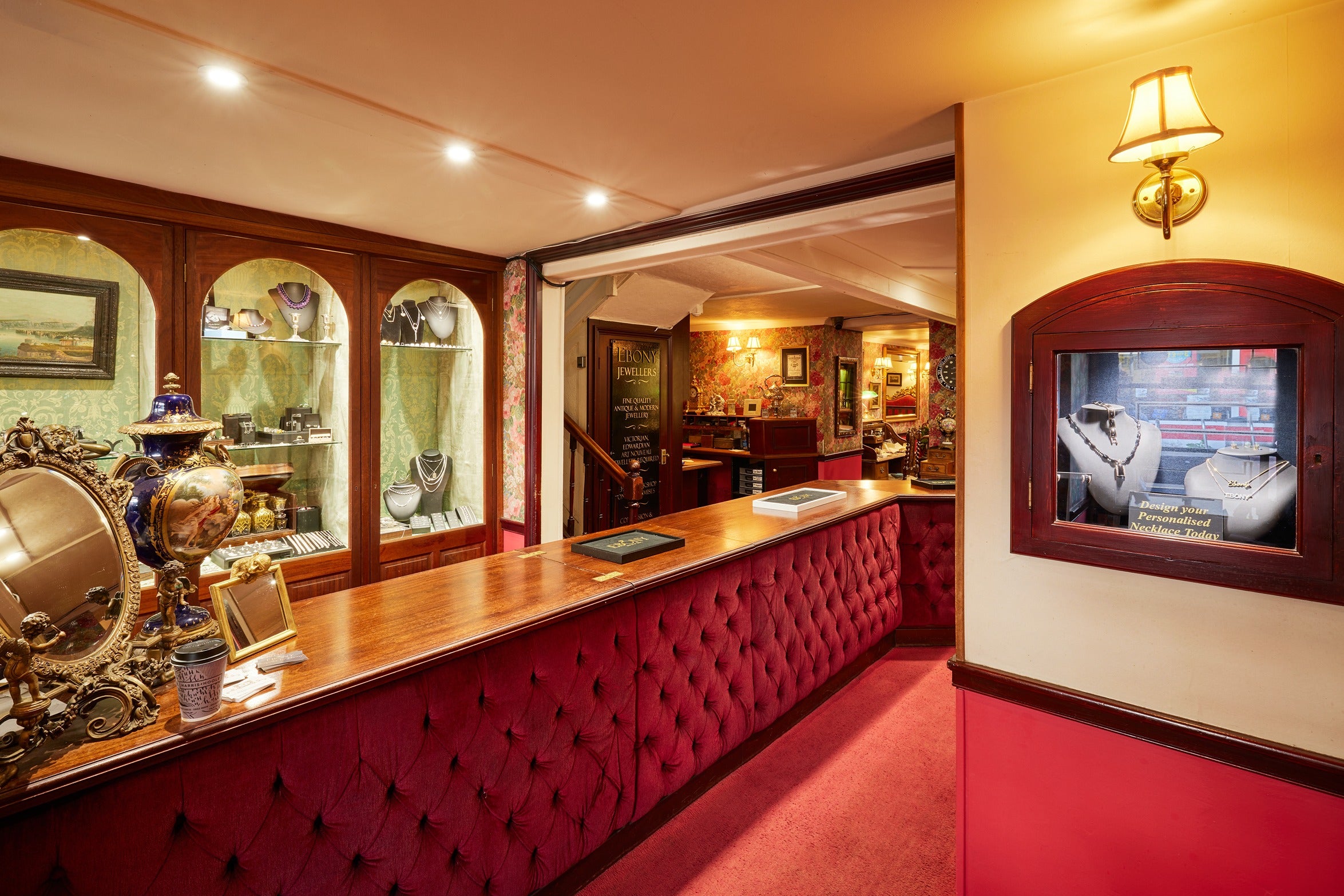 A wide shot of the main service area, showing a long, deep red tufted velvet counter. Large arched built-in display cases behind the counter house a vast collection of necklaces and fine jewellery.