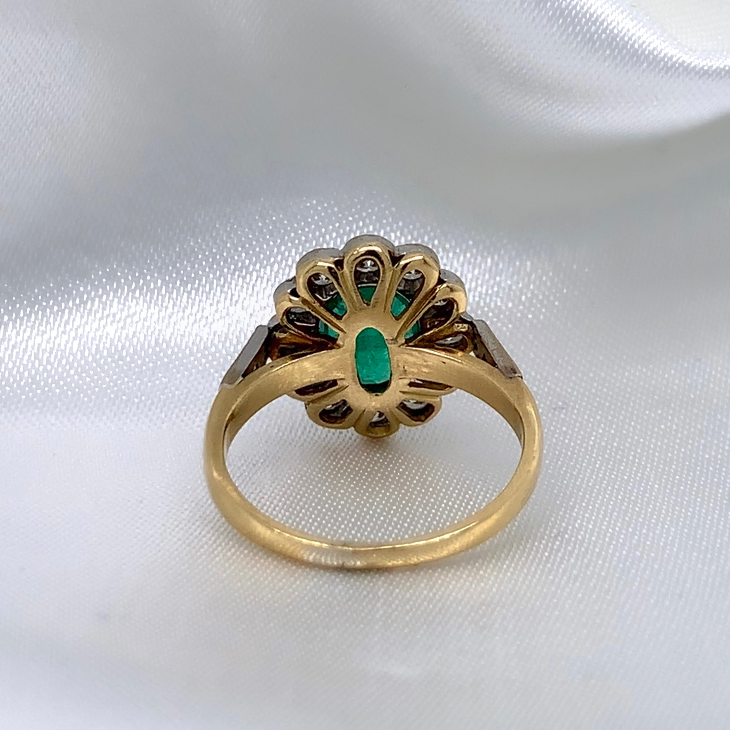 A back view of a 1940s emerald and diamond cluster ring with a classic Art Deco design, featuring a central emerald surrounded by a halo of diamonds.