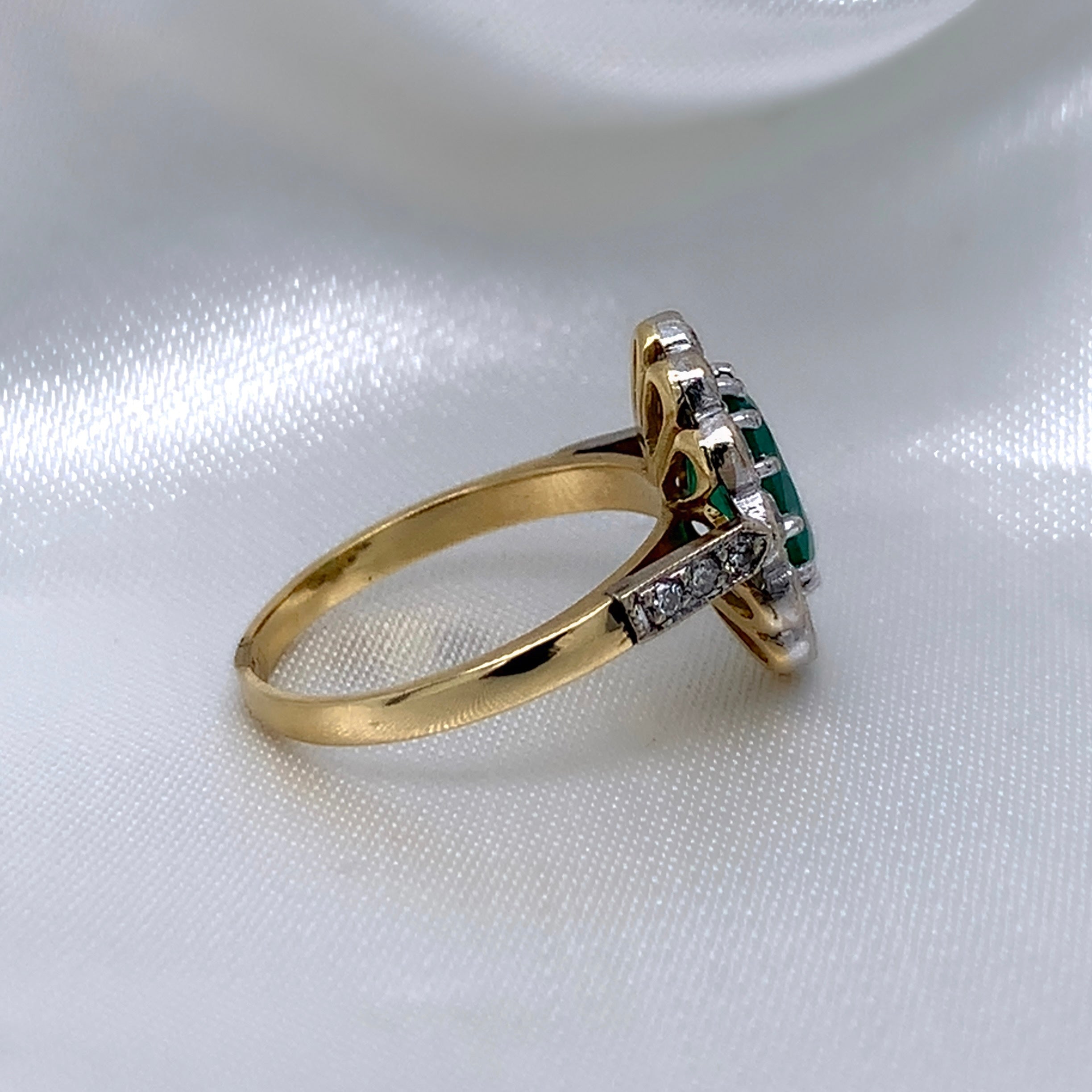 A side view of a 1940s emerald and diamond cluster ring with a classic Art Deco design, featuring a central emerald surrounded by a halo of diamonds.
