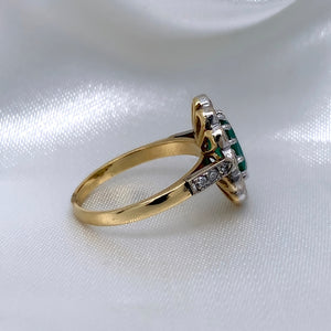 A side view of a 1940s emerald and diamond cluster ring with a classic Art Deco design, featuring a central emerald surrounded by a halo of diamonds.