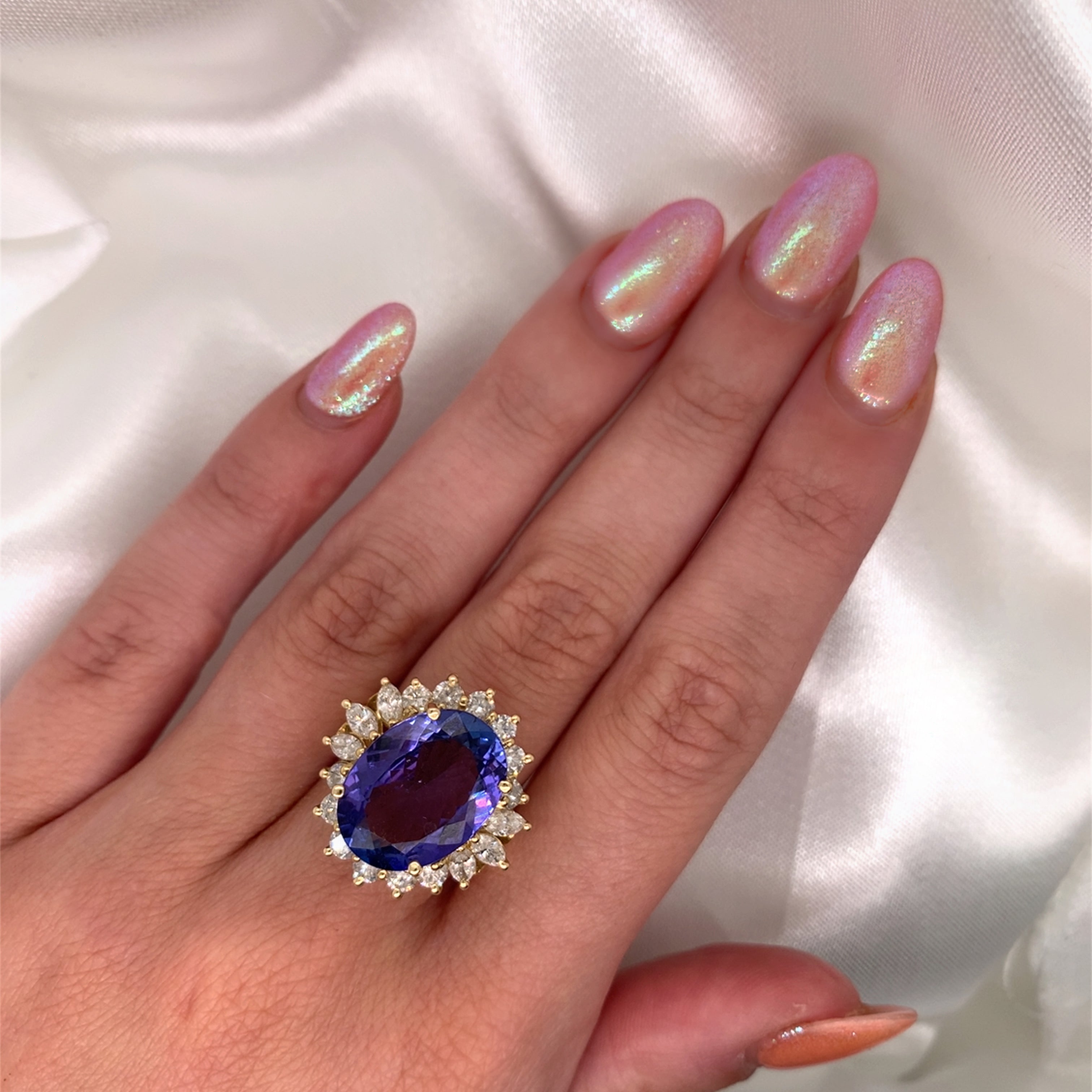 A stunning cocktail ring with a large oval-cut sapphire surrounded by a halo of sparkling diamonds,  set in yellow gold modelled on a hand.