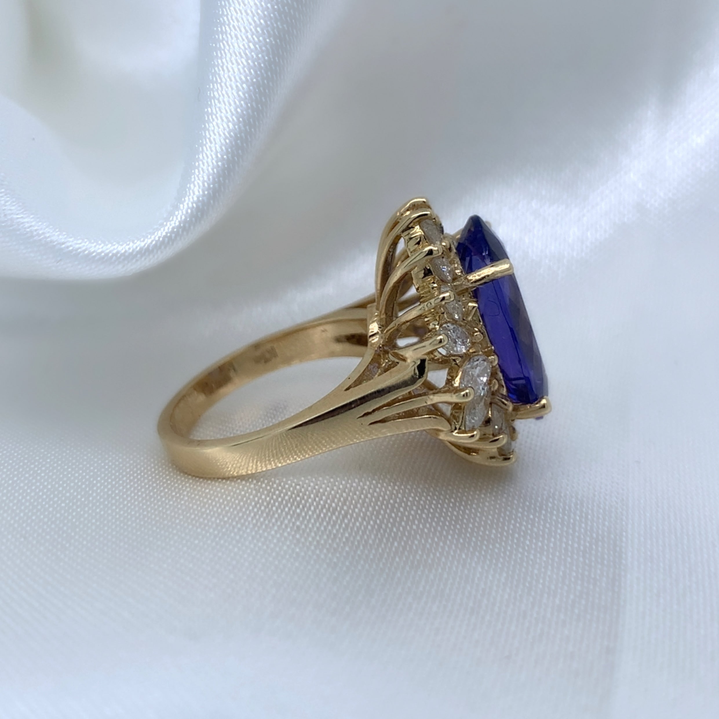 The side of a stunning cocktail ring with a large oval-cut sapphire surrounded by a halo of sparkling diamonds,  set in yellow gold.
