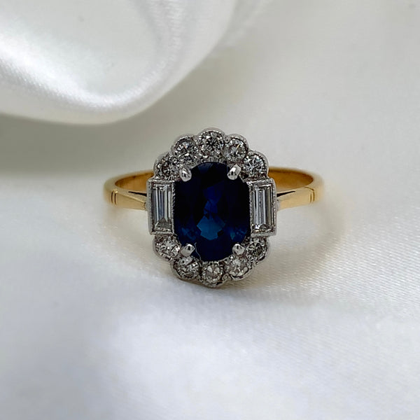 1980s Art Deco ring with a deep blue oval-cut sapphire surrounded by a halo of sparkling diamonds featuring a vibrant sapphire and a platinum and 18ct yellow gold setting