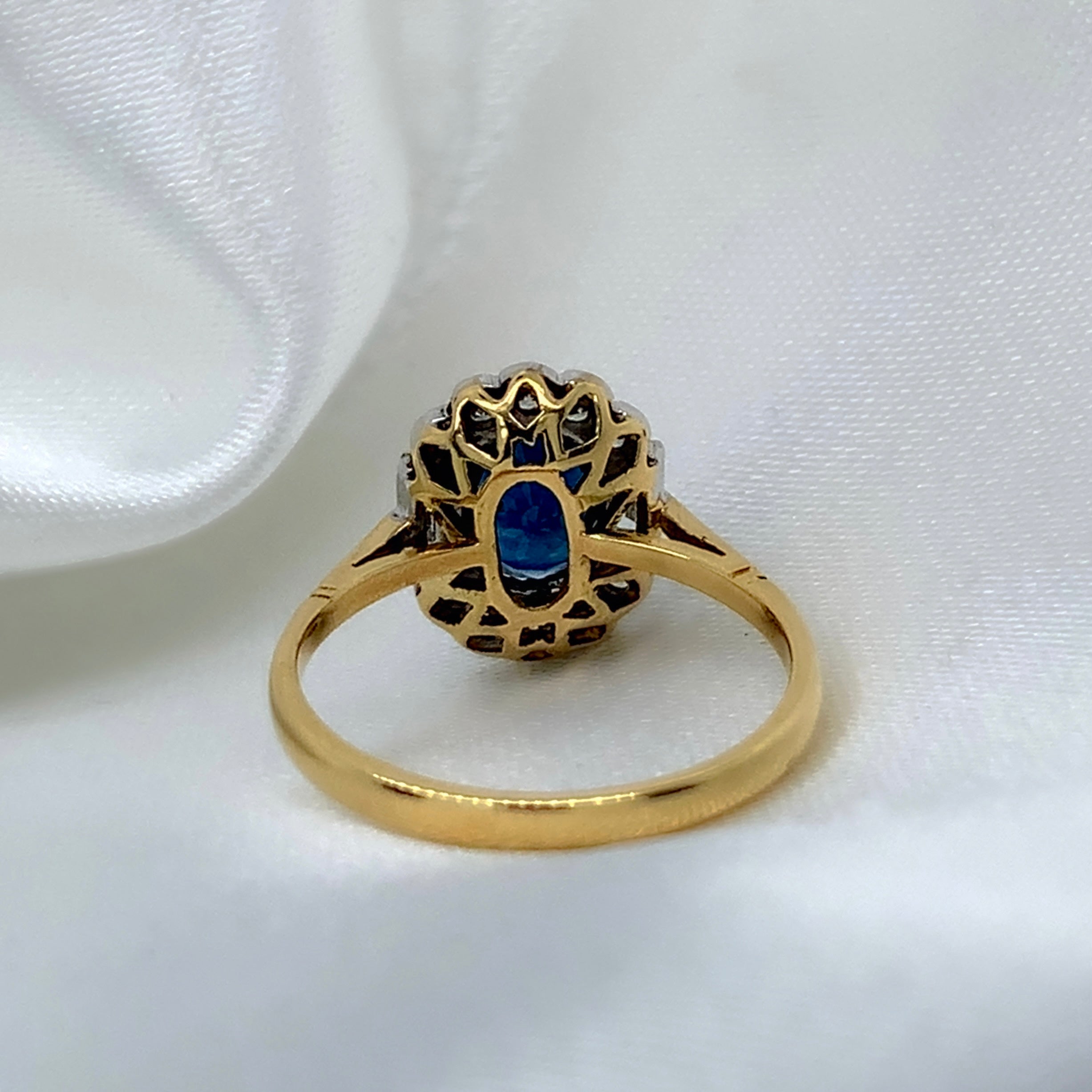 A back view of a 1980s Art Deco ring with a deep blue oval-cut sapphire surrounded by a halo of sparkling diamonds featuring a vibrant sapphire and a platinum and 18ct yellow gold setting