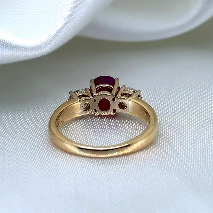 A back view of a 18k yellow gold three-stone ring featuring a vibrant oval-cut ruby surrounded by two sparkling round brilliant diamonds.