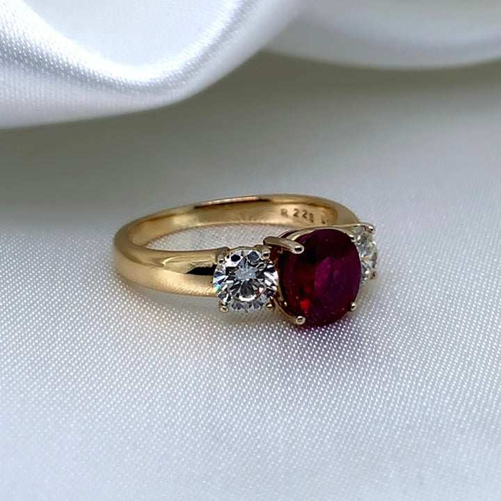 A side view of a 18ct yellow gold three-stone ring featuring a vibrant oval-cut ruby surrounded by two sparkling round brilliant diamonds.