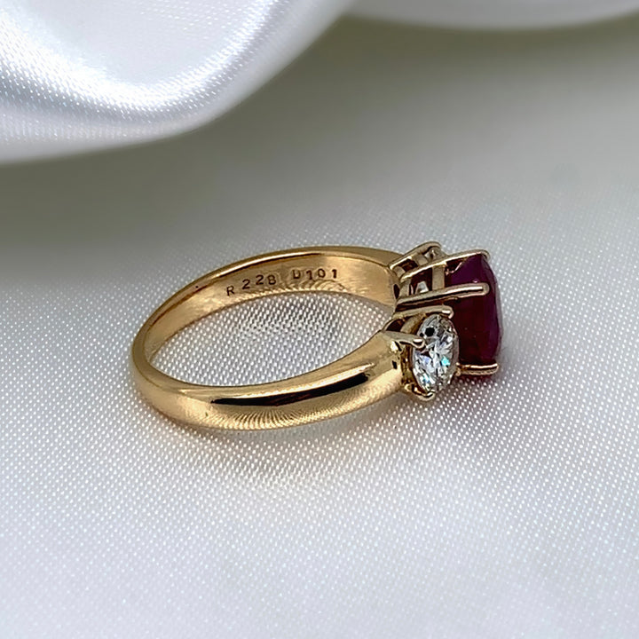 A side view of a 18ct yellow gold three-stone ring featuring a vibrant oval-cut ruby surrounded by two sparkling round brilliant diamonds.