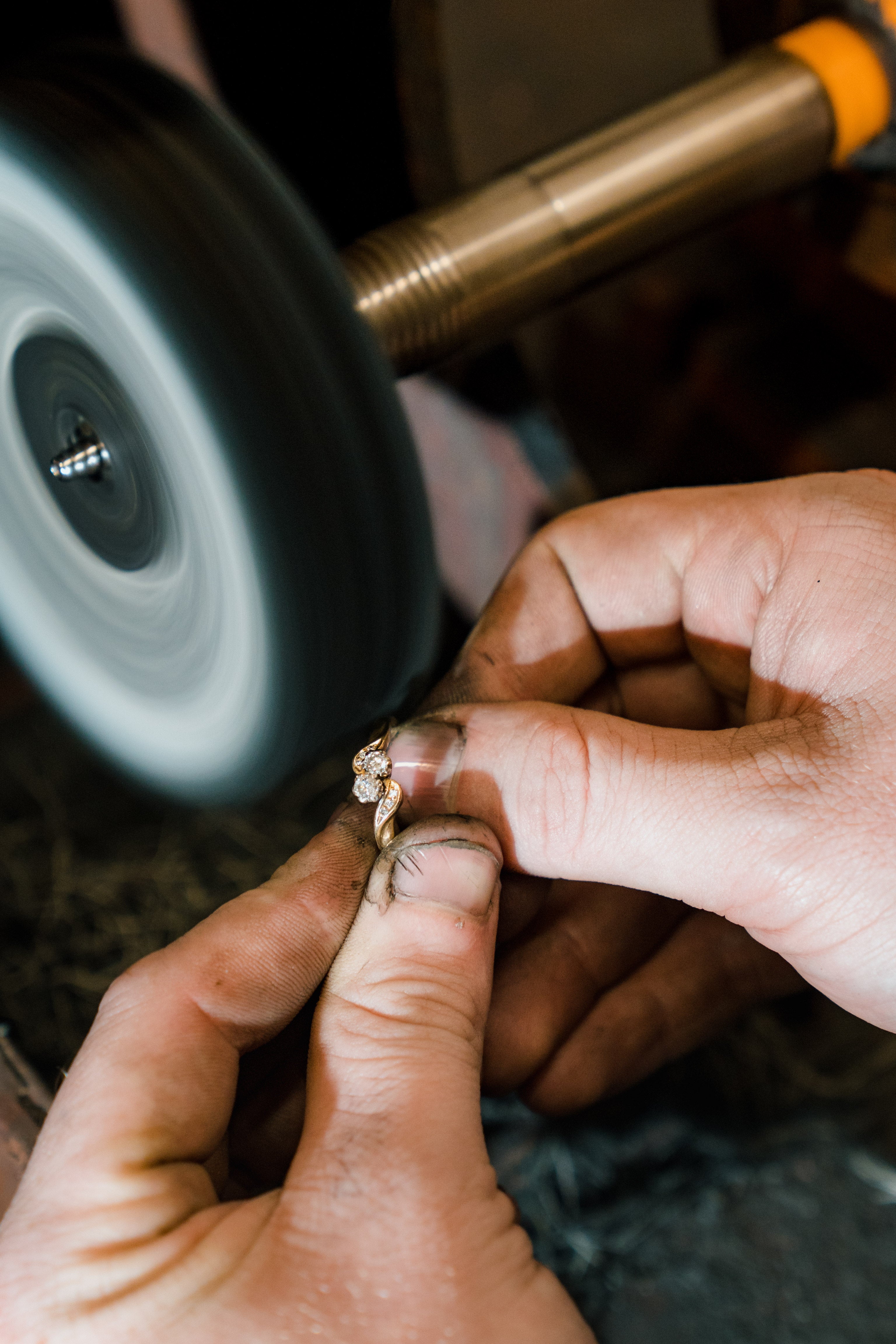 A close-up of the jewellery repair and restoration process, showing a craftsman’s hands holding a gold diamond ring against a spinning polishing wheel to restore its original luster and shine.